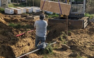 Stone retaining wall being built to terrace the slope behind one of the buildings and stop further sliding.