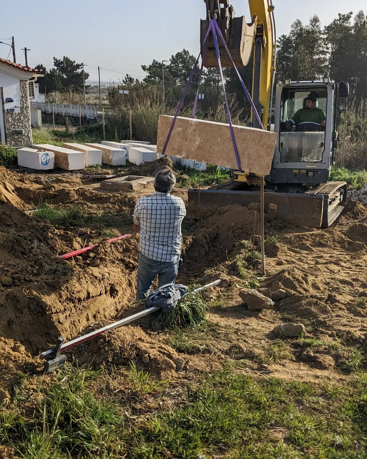 Stone retaining wall being built to terrace the slope behind one of the buildings and stop further sliding.